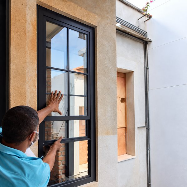 Instalador da Maxwell encaixando uma janela de alumínio preto no vão de uma obra